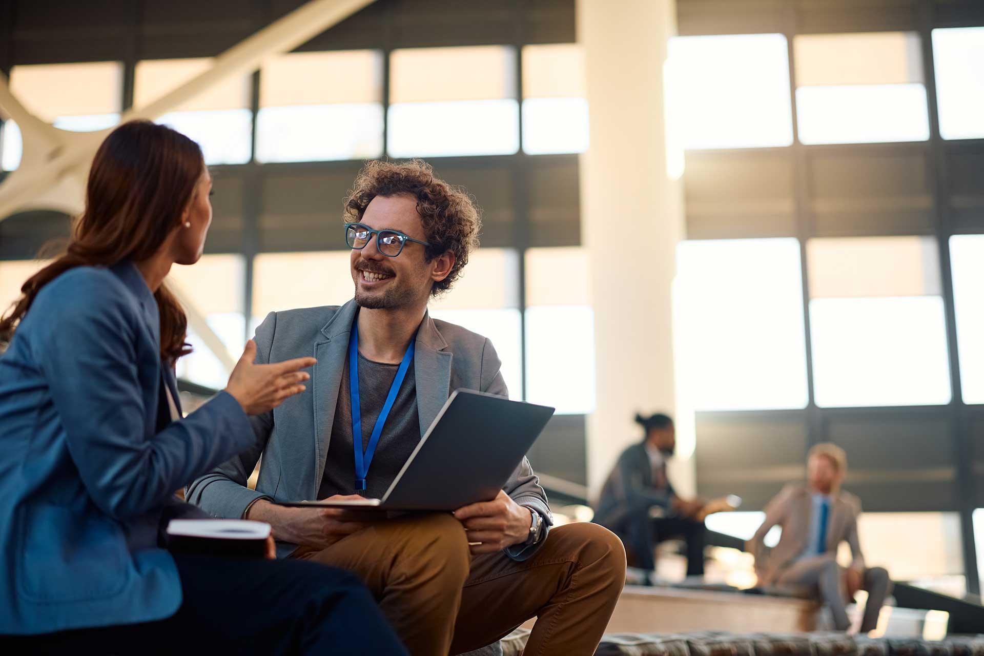 Two professional services colleagues in conversation over a laptop in an office atrium